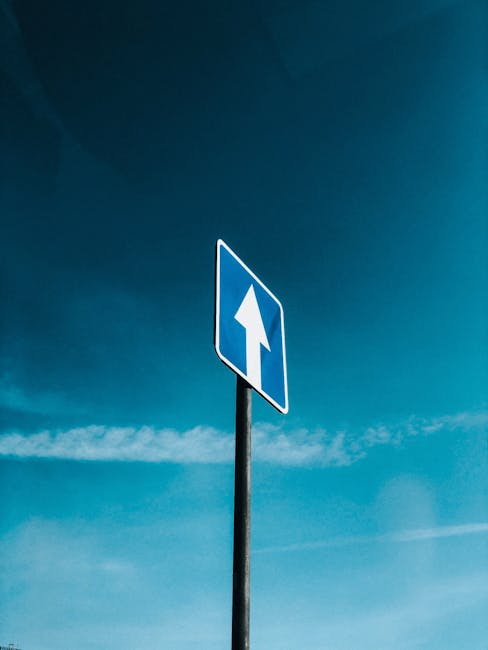 A blue traffic sign with an upward arrow against a clear blue sky, symbolizing direction and movement.